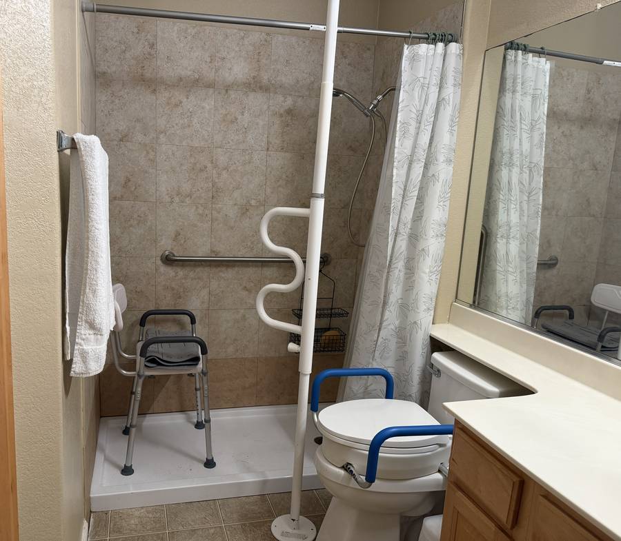 Bathroom with walk-in shower, grab bars, shower chair, support pole and raised toilet seat