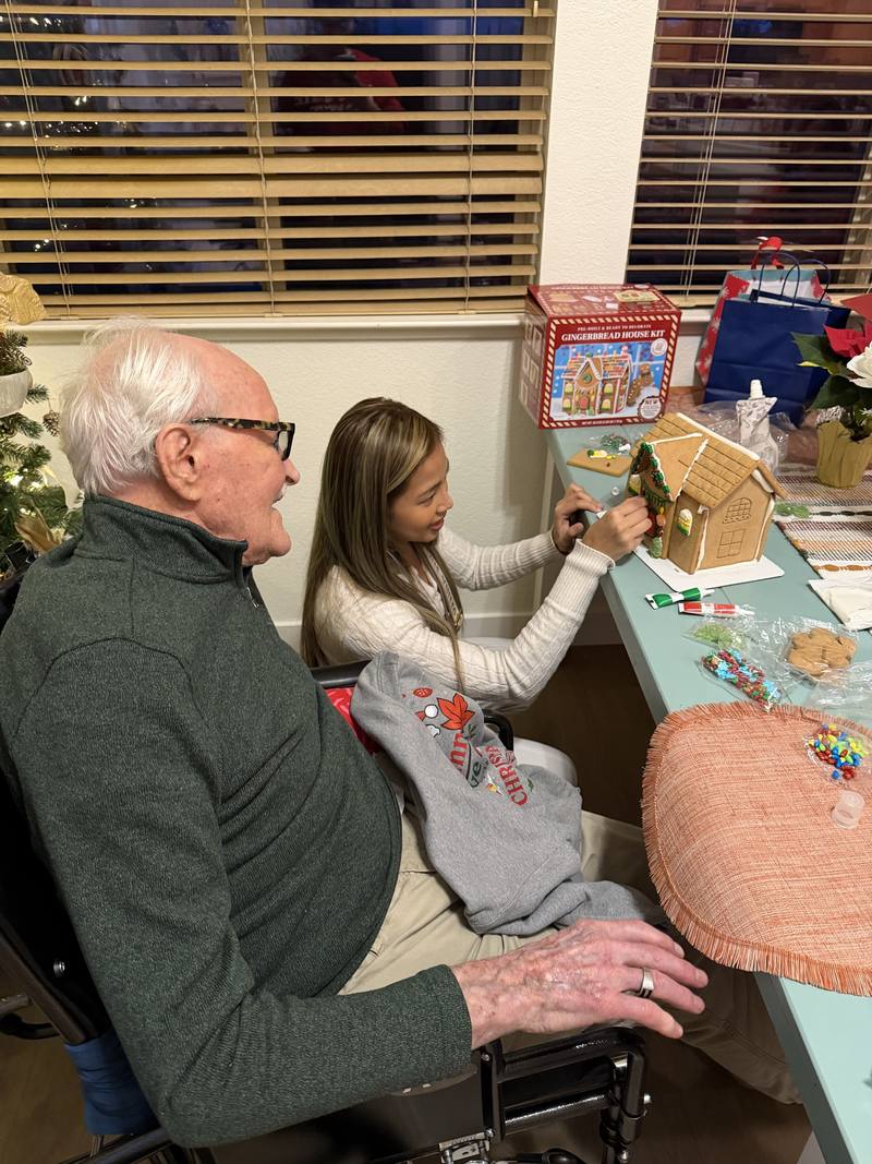 A caregiver decorating a gingerbread house with a resident