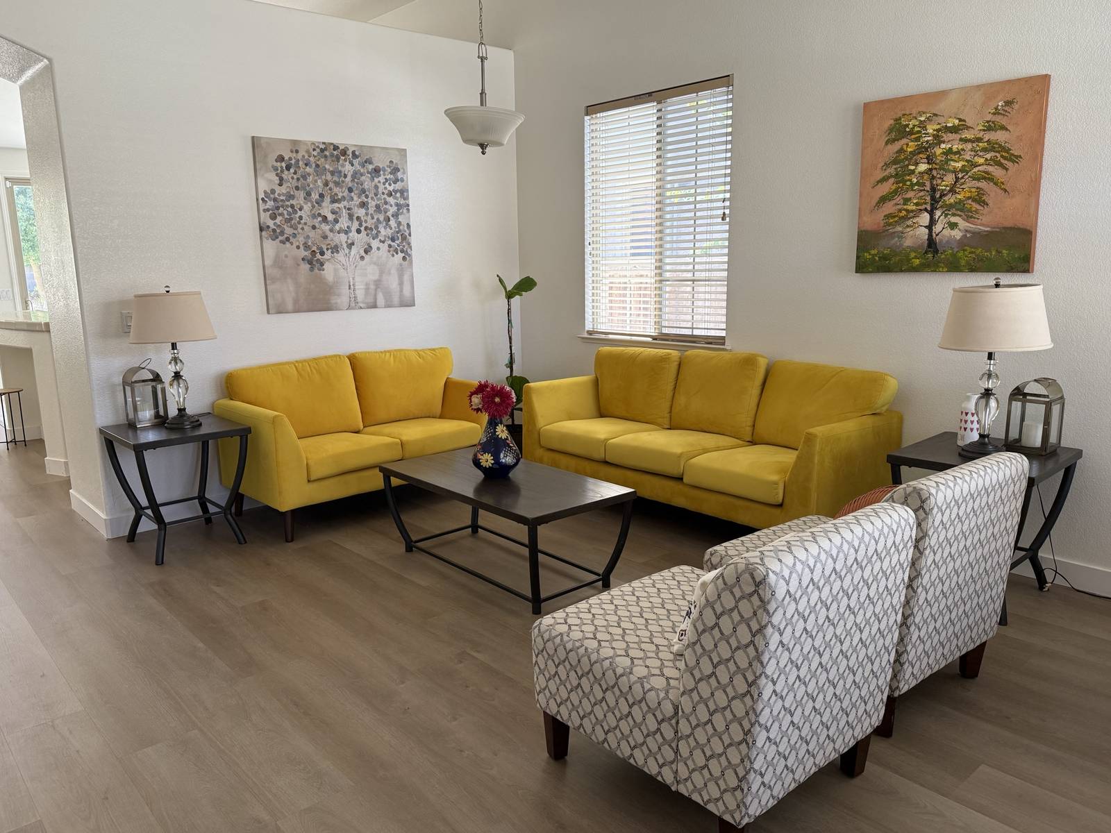 Bright living room with two yellow sofas, armchairs and tree paintings
