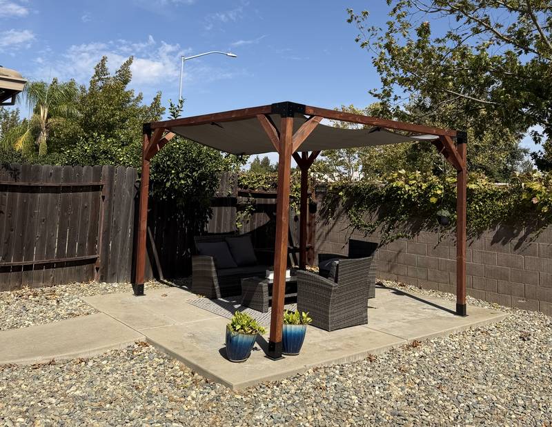 Shaded wooden pergola with outdoor sofa and chairs in the backyard
