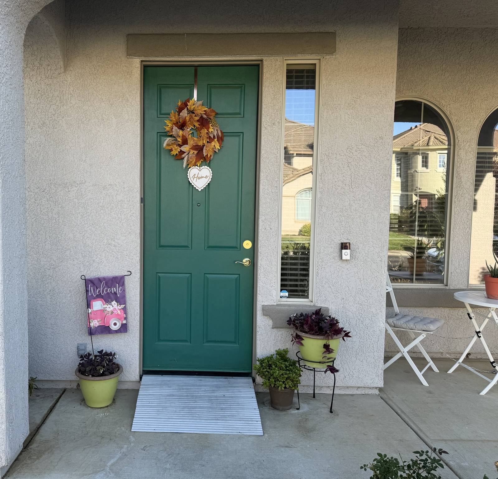 Covered front porch with a green door, fall wreath and bistro table