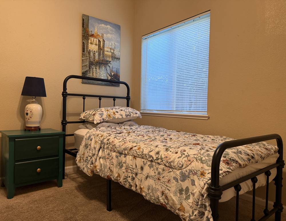 Private room with an iron bed, floral comforter, green nightstand and window