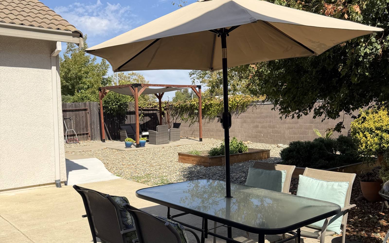 Backyard patio dining table with the pergola and garden beds behind